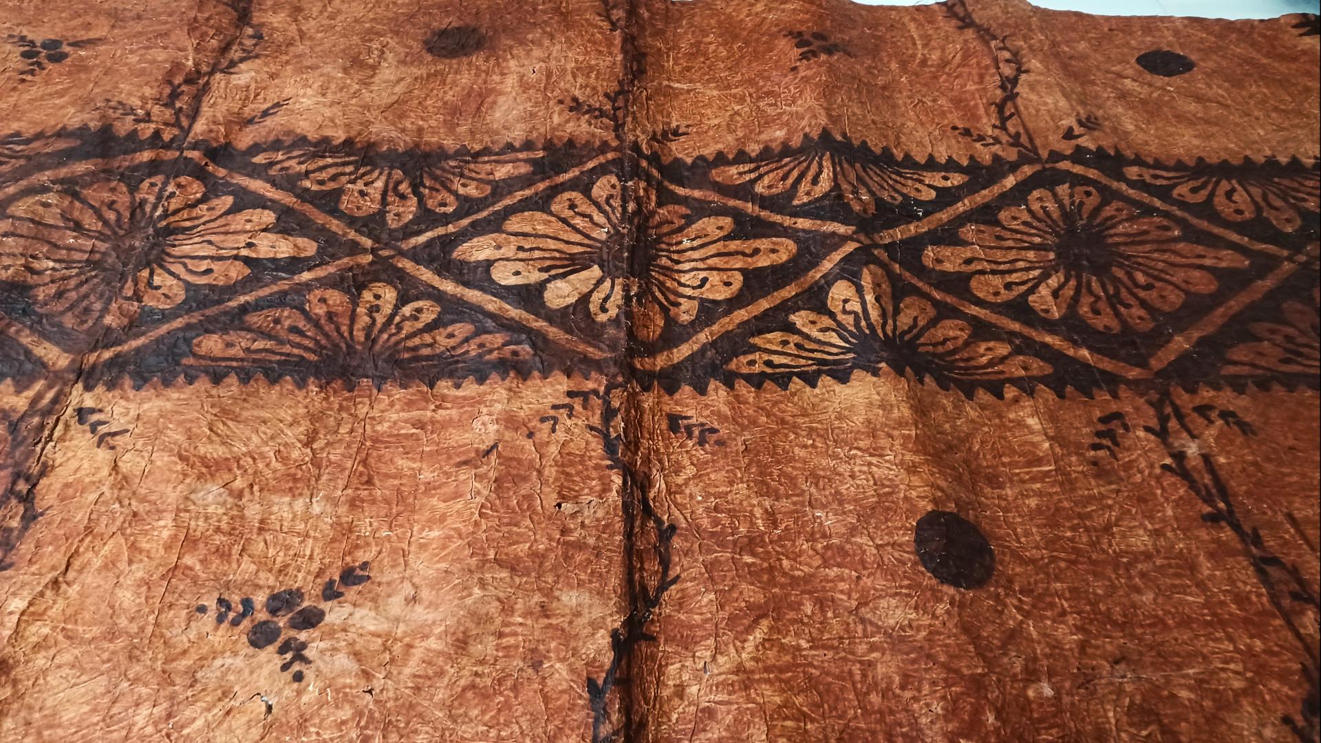 Tapa o pieza textil proveniente de Tonga, confeccionada por las fibras de mahute, con diseños de tonalidades cafés. 