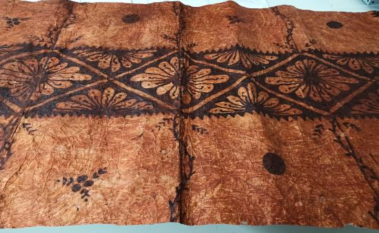 Tapa o pieza textil proveniente de Tonga, confeccionada por las fibras de mahute, con diseños de tonalidades cafés. 